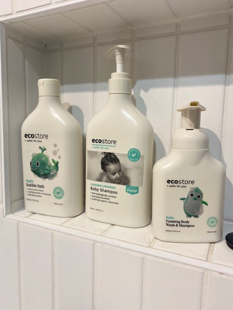 three ecostore bottles containing baby wash, shampoo and bath soap itting on a bath niche shelf.