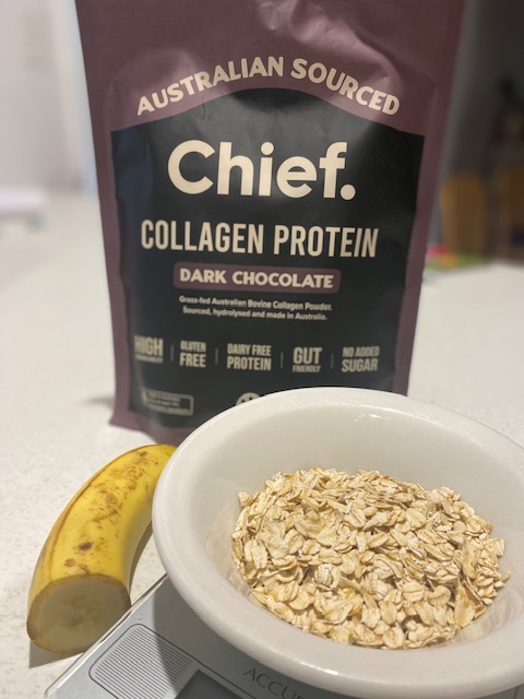 A bowl of rolled oats sits on a kitchen scale next to a ripe banana, with a package of Chief Collagen Protein powder in the background, showcasing its dark chocolate flavor.